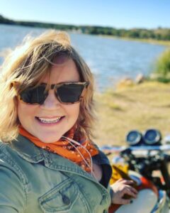 lady with sunglasses on a motorcycle next to a lake
