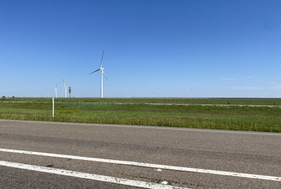Paved road with green grass and large windmill farm in the background