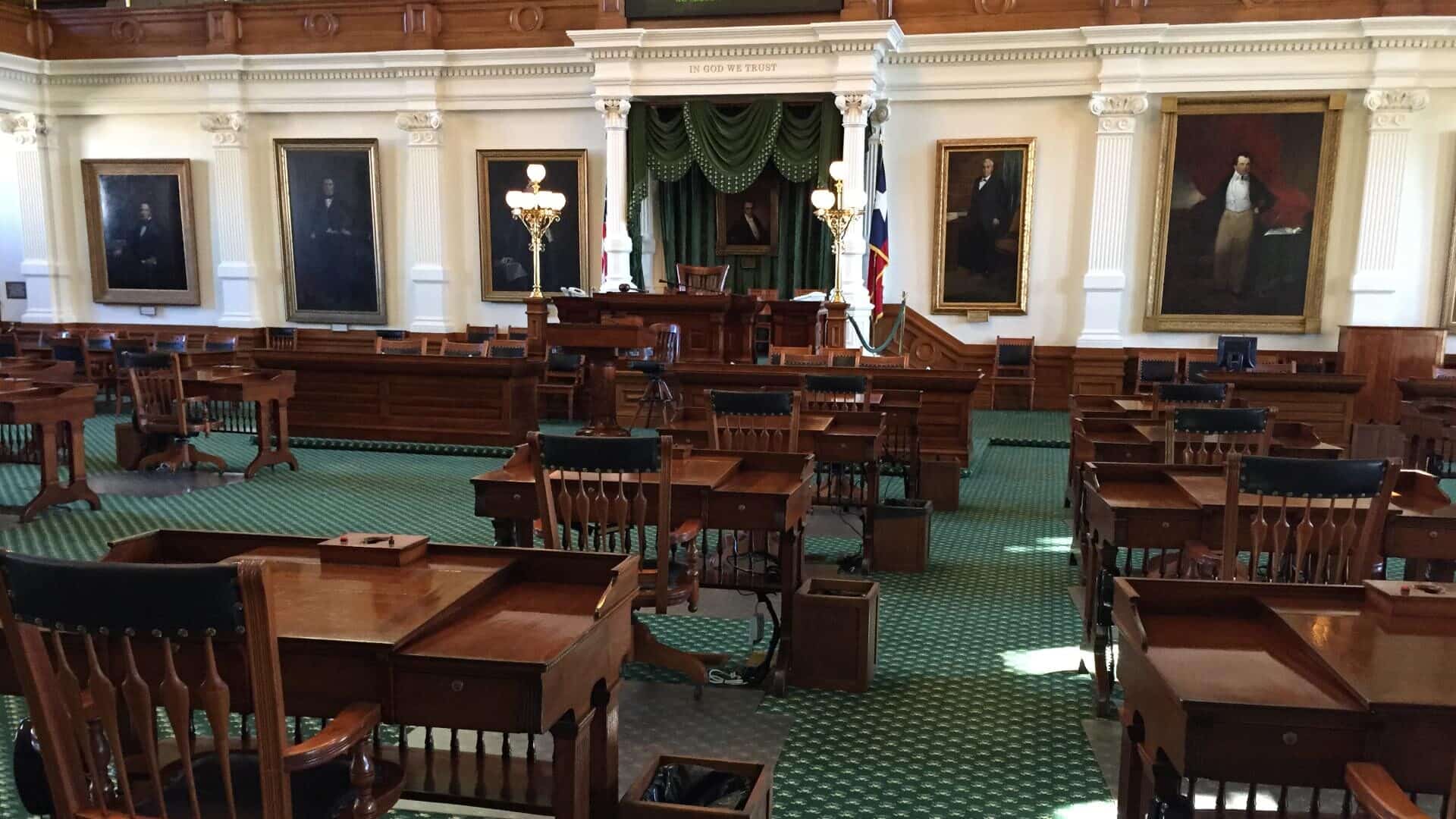 Large room with green carpet and dark wooden desks and chairs at a Capitol building