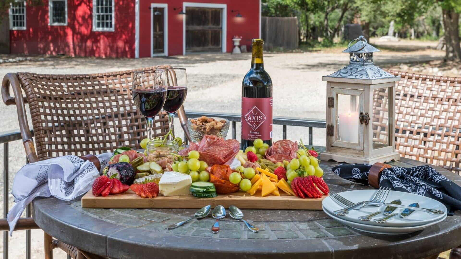 Fully loaded charcuterie board with meats, cheeses, fruits, and nuts and two glasses of red wine on a round table