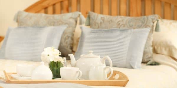Close up view of wooden tray with white teapot set on bed